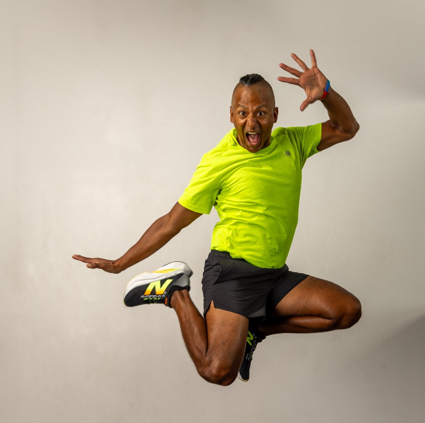 Stiva mid-air in a high-energy jump in a gym, one hand raised, wearing a neon lime shirt